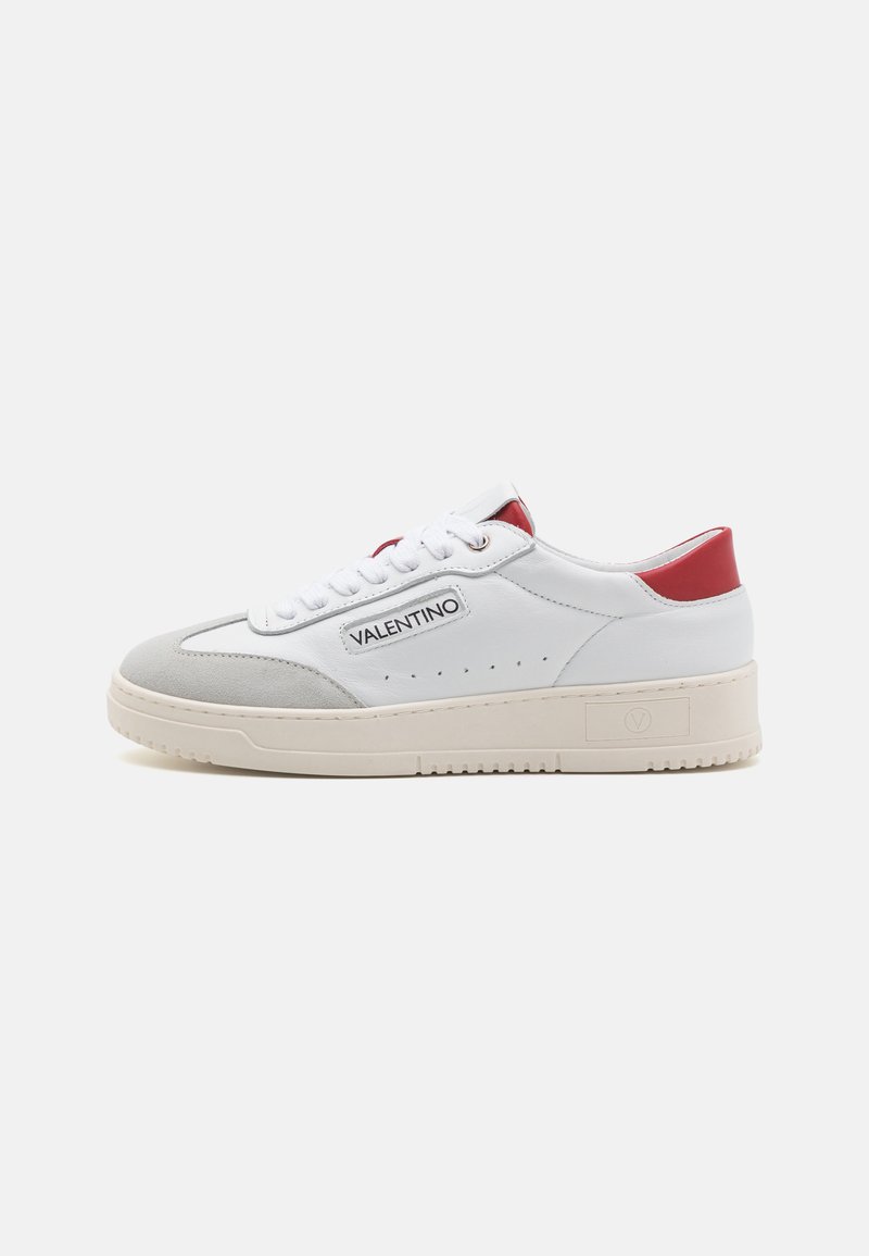 Sneaker bianco in pelle con tallone rosso a contrasto, dettagli in suede grigio, traforature sui lati e suola spessa beige. Presenta un logo laterale.