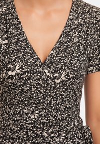 Detailní záběr na osobu v černo-bílé květinové zavinovací šaty s krátkými rukávy a výstřihem do V.