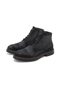 Botas de ante negras hasta el tobillo con punta redondeada, cordones en la parte delantera y costuras decorativas. Presenta una parte superior texturizada y una suela marrón de contraste.
