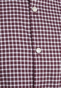 Tessuto a quadri bordeaux e bianco con due bottoni bianchi allacciati lungo la patta centrale.