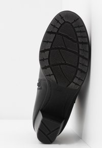 Semelle de chaussure noire avec un dessous en caoutchouc texturé présentant un motif de bande de roulement pour l'adhérence, un design courbé et un talon renforcé.