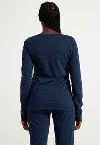 Haut de pyjama à manches longues bleu marine avec un col arrondi et de petits points métalliques dispersés ; associé à un pantalon assorti pour un ensemble cohérent.