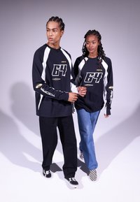 Black long-sleeve shirts with white accents, featuring bold "64" graphic. Models wear black pants and checkered sneakers, holding hands.