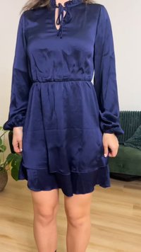 Tengerészkék szatén ruha hosszú gombócos ujjakkal, fodros nyakkivágással, derékban megkötős, és réteges szoknyavéggel. Simogató textúra, elegáns dizájn.