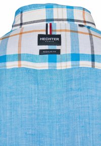 Blauw geruit shirt met een wit, blauw en oranje ruitenpatroon op de kraag. Bevat een zwart merklabel met "HECHTER PARIS" en "REGULAR FIT."