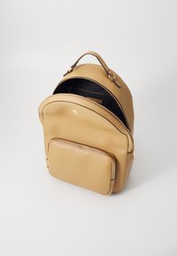 Tan-farbener Leder-Rucksack mit runder Form, ausgestattet mit einem Hauptfach mit Reißverschluss, einer vorderen Reißverschlusstasche und dezentem goldfarbenem Logo. 