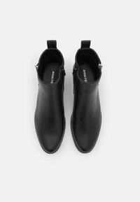 Paire de bottines en cuir noir avec fermetures éclair latérales et languettes, vue de dessus sur fond blanc.