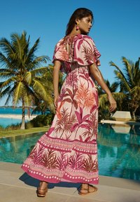 Rochie maxi roz cu un model de frunze tropicale și mâneci enhance. Detaliu legat în spate, accentuat cu un tiv imprimat. Purtați cu sandale plate.