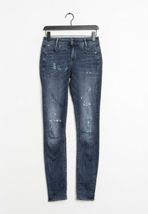 Jean skinny bleu foncé avec un délavage passé, présentant des patches déchirés et un design classique à 5 poches. Fabriqué en tissu denim.