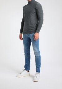 Harmaa neulepusero, jossa on korkea kaulus ja ribbireunat, yhdistettynä vaaleansinisiin slim-fit-farkkuihin ja valkoisiin tennareihin, joissa on mustia yksityiskohtia.