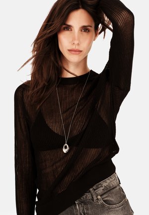 Jersey negro de punto con un tejido abierto, mangas largas, escote redondo, combinado con jeans grises y un collar de pendant de plata.