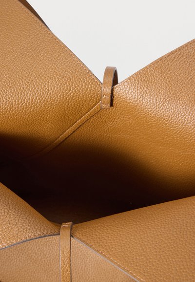 Ανοιχτή τσάντα από μαλακό δέρμα ταμπά που δείχνει την υφή εσωτερικά και δύο δερμάτινες θηλιές στις άκρες του ανοίγματος σε λευκό φόντο.