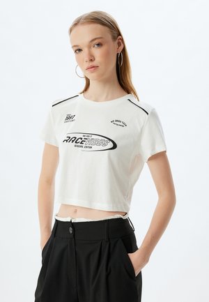 Weißes, kurz geschnittenes T-Shirt mit schwarzem Text und grafischen Designs, mit kurzen Ärmeln und kontrastierenden schwarzen Akzenten auf den Schultern.