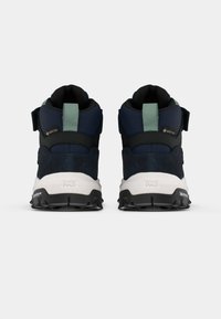 Buty trekkingowe z granatową cholewką, wyściełaną czarną podeszwą, etykietą GORE-TEX i jasnoniebieskimi akcentami. Posiadają wyściełany kołnierz oraz regulowane paski.