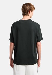 Camiseta de algodón negra con un corte relajado, mangas cortas y cuello redondo. Textura suave y diseño sencillo sin logotipos ni estampados.