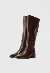 Botas de cuero marrón hasta la rodilla con un acabado suave, punta ligeramente afilada y un tacón bajo en bloque para mayor estabilidad. Presentan un diseño ajustado.