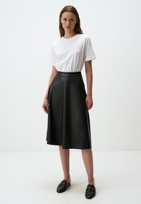 Jupe midi en cuir noir avec une texture lisse et un design en A, associée à un t-shirt en coton blanc et des mocassins noirs.