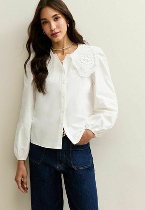 Witte katoenen blouse met een decoratieve kraag van kant, knopen aan de voorkant, pofmouwtjes en een relaxte pasvorm, gestyled met donkere denim jeans.
