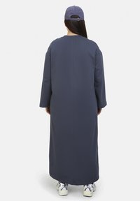 Navy long-sleeve dress with a relaxed fit and round neckline, paired with a light purple cap and white sneakers. Smooth fabric texture.