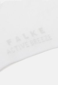 Hvit tekstilmerkelapp med preget merkevare "FALKE ACTIVE BREEZE." Glatt tekstur, rektangulær form, minimalistisk design, ingen ekstra mønstre.