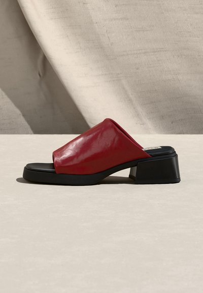 Κόκκινο δερμάτινο mule με ανοιχτά δάχτυλα, μαύρο χαμηλό τακούνι τύπου block και επενδεδυμένο πάτο, εμφανίζεται σε πλάγια όψη σε ουδέτερο υφασμάτινο φόντο.