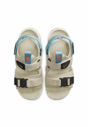 Beżowe i niebieskie sandały Nike z regulowanymi paskami, czarnymi klamrami i pomarańczowymi akcentami logo, widziane z góry.