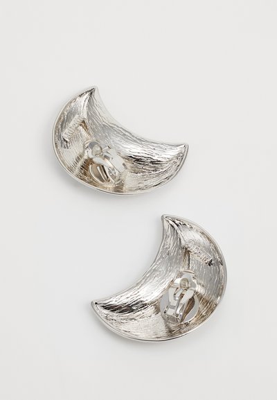 Boucles d'oreilles en forme de croissant en argent, avec une surface texturée et des fermoirs à clip, présentant un intérieur lisse et une finition réfléchissante.