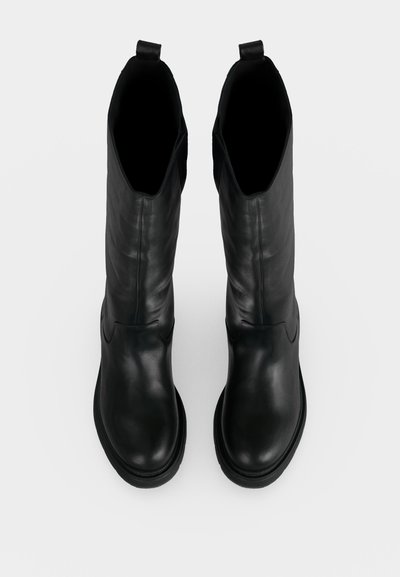 Paire de bottes en cuir noir mi-mollet avec bouts ronds et languettes en haut, vues de dessus sur fond blanc.