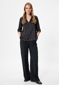 Zwarte, zijden blouse met een v-hals en opgerolde mouwen, gecombineerd met loszittende zwarte broeken. Doorzichtige textuur en een gladde afwerking.