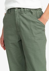 Pantalon en coton vert à coupe d écontractée, avec poches latérales et un détail bouton à la taille pour une fonctionnalité accrue.