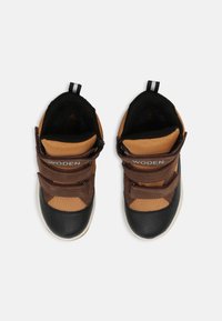 Tênis castanhos e pretos com parte superior em malha e couro, duas tiras de velcro, sola de borracha, colarinho acolchoado e alça na parte traseira para facilitar o calçar.