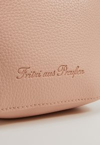 Světle růžová texturovaná kožená kabelka s raženým logem "Fritzi aus Preußen", s jemným prošíváním podél okraje.