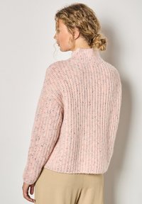 Różowy sweter prążkowany z wysokim kołnierzem i długimi rękawami, wykonany z teksturowanej włóczki z subtelnymi, wielokolorowymi fleckami.