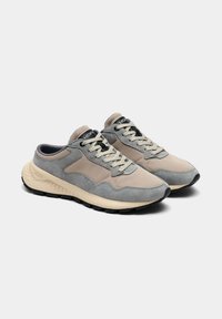 Baskets en daim gris et beige avec une semelle texturée, présentant un bout arrondi, des lacets contrastants et un col rembourré pour un confort accru.