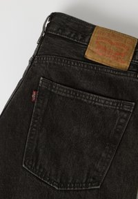 Πίσω τσέπη και μέση μαύρου τζιν Levi's με ορατή κόκκινη ετικέτα Levi's και καφέ δερμάτινο λογότυπο.