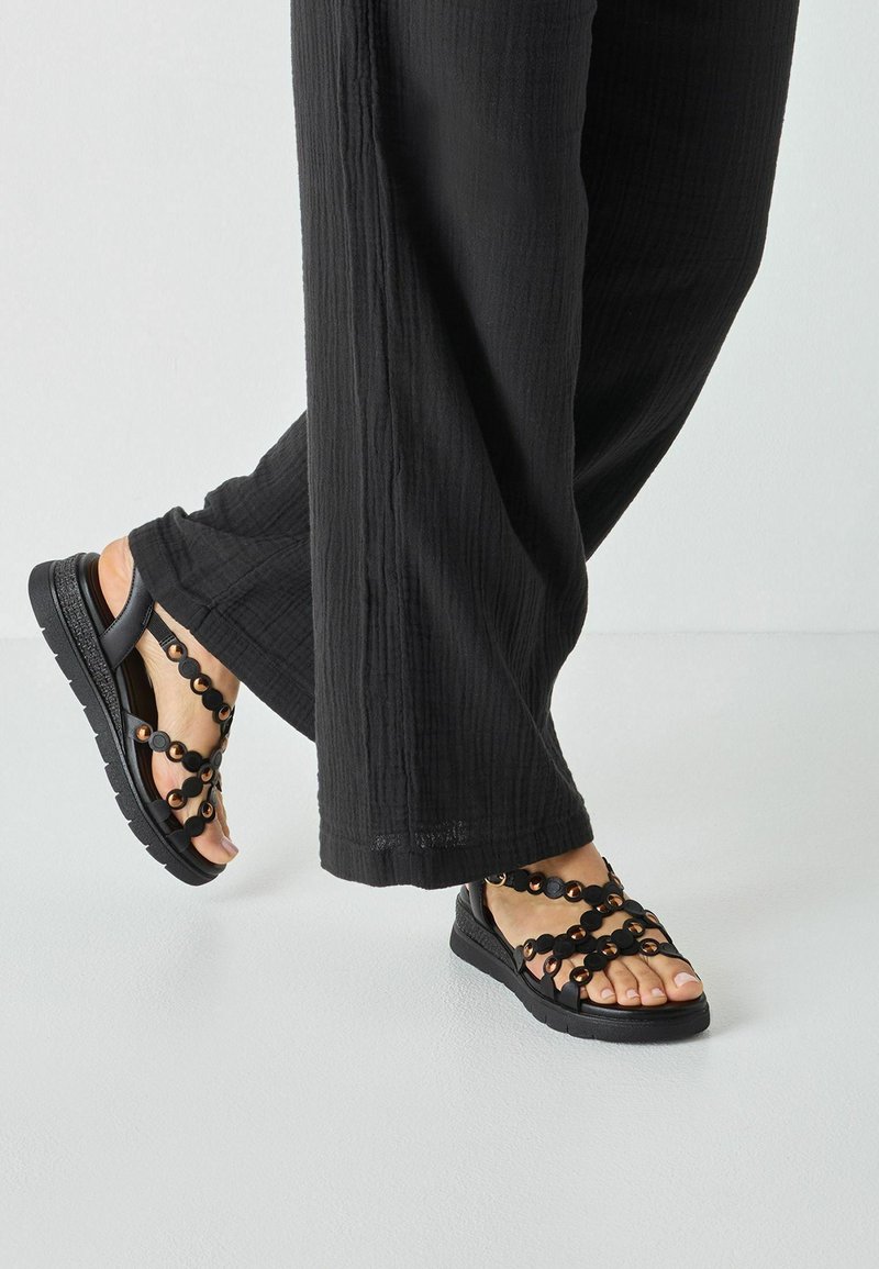Sandales noires avec des accents circulaires et un design de sangle texturée, dotées d'une semelle rembourrée et d'une tige flexible pour le confort.
