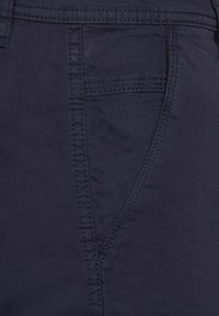 Tejido de color azul marino con una textura suave, que presenta un bolsillo lateral y detalles cosidos, resaltando un diseño ajustado adecuado para uso casual.