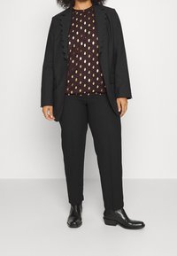 Blazer nero con bordi scallop, top bordeaux a fantasia con accenti dorati a forma di foglia, pantaloni neri su misura e stivali alla caviglia neri eleganti.