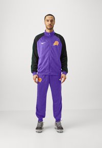 Fialový športový teplákový komplet s čiernymi rukávmi. Obsahuje logo basketbalu a zelené akcenty. Nohavice sú rovné s elastickými manžetami.