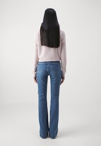 Sudadera rosa clara con capucha, combinada con jeans acampanados azules que cuentan con un diseño de cinco bolsillos y detalles de costura visibles.