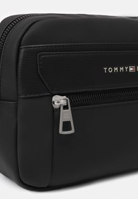 Bolsa de cosméticos rectangular negra con una superficie suave, acentos texturizados, herrajes de cremallera plateados y detalle de logo en relieve.