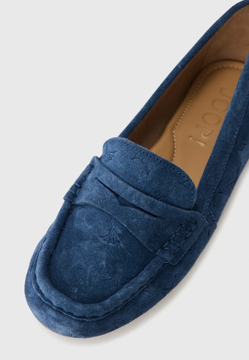 Marineblaue Wildlederslipper mit einem geprägten Design, genähten Details und einer abgerundeten Zehenpartie. Das Innere ist mit einem glatten, hellbraunen Material ausgekleidet.