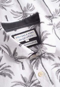 Camicia a maniche corte in tessuto bianco con stampa di palme nere. Presenta un colletto con bottoni e un'etichetta tessuta con informazioni sul marchio.