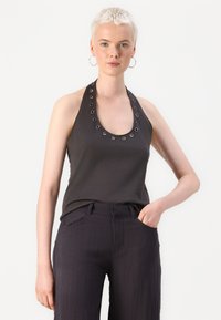 Crna halter top majica s detaljima od metalnih grometa oko izreza, izrađena od mekanog materijala. Uparena s tamnim, teksturiranim hlačama širokih nogavica.