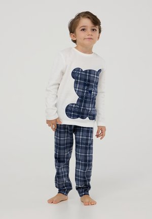 Pigiama bianco a maniche lunghe con grafica di un orsetto di peluche blu navy. Pantaloni del pigiama a quadri blu navy e grigi. Tessuto morbido, vestibilità comoda, senza motivi visibili.