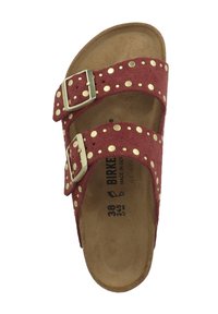 Rode vilten sandalen met twee verstelbare banden, versierd met gouden studs, en een kurken voetbed. Voorzien van metalen gespen voor aanpassing.