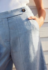Pantalons en lin bleu clair avec un motif en chevrons, taille haute, poches latérales et fermeture à boutons à l'avant.