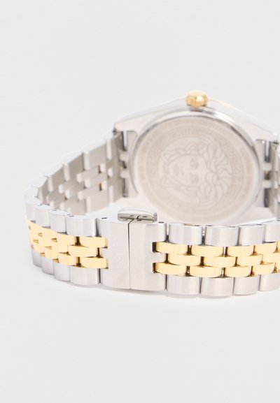 Ασημένια και χρυσή μεταλλική μπάντα ρολογιού με αγκράφα, που δείχνει την πίσω πλευρά της θήκης του ρολογιού χαραγμένη με σχέδιο προσώπου.