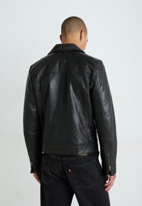 Must olla must nahast jope, millel on sobiv disain, lai krae ja tõmblukuga mansetid. Sile tekstuur ja peene läikega, koos mustade teksadega.