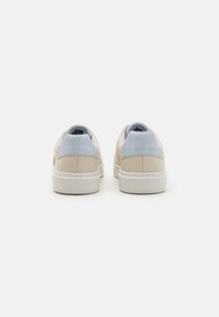 Beige sneakers med en jevn finish, med lyseblå detaljer ved hælen og en hvit gummisåle med sømdetaljer.